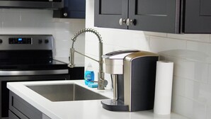 Una cocina moderna con armarios oscuros, electrodomésticos de acero inoxidable y encimera blanca.