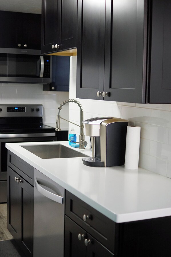 Una cocina moderna con armarios oscuros, electrodomésticos de acero inoxidable y encimera blanca.