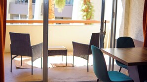 Un balcón con sillas de mimbre y una mesa de madera, con vista a un edificio que tiene un balcón y palmeras.