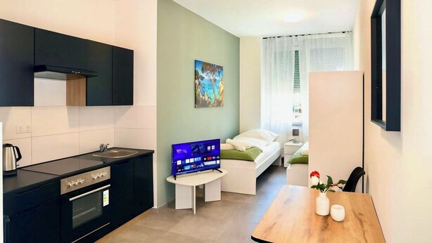 A compact kitchen with modern appliances, a dining area with a wooden table, and a bedroom with a bed and a nightstand. - City apartment no. 13 with comfort (Pforzheim)