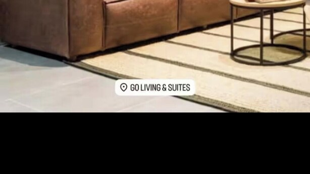 A modern living room with a brown leather sofa, two round mirrors on the wall, and a small round table with a book.