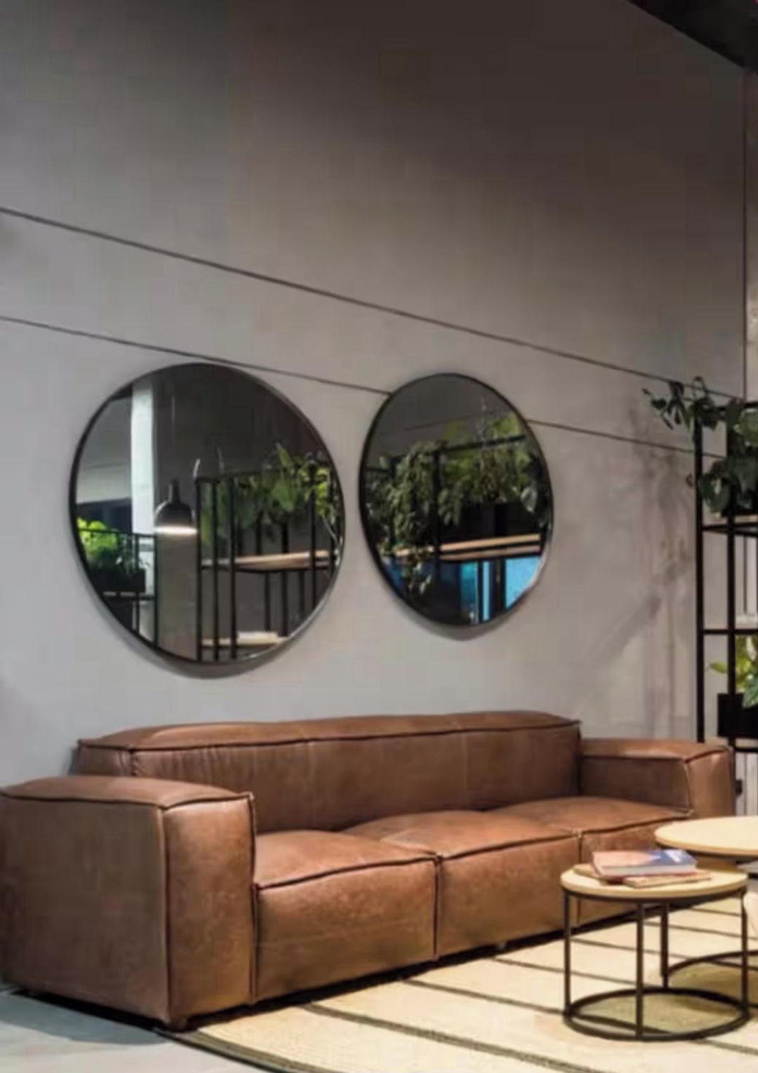 Un salon moderne avec un canapé en cuir marron, deux miroirs ronds accrochés au mur et une petite table ronde sur laquelle repose un livre.