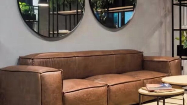 Uma sala de estar moderna com um sofá de couro marrom, dois espelhos redondos na parede e uma pequena mesa redonda com um livro.