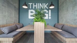 A modern meeting room with a wooden table, two grey cushioned benches, and a large wall-mounted sign that reads "THINK BIG!".