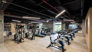 A gym with multiple exercise machines, wooden flooring, and exposed ductwork on the ceiling.
