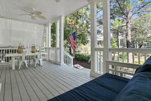A covered porch with a white railing, a table with chairs, and an American flag. - Liberty Point 4BR/3.5BA Home | Golf Cart, Bikes & Resort Amenities | NatureWalk 30A (Santa Rosa Beach)