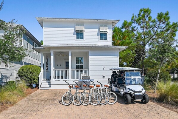 A two-story white house with a porch, a covered patio, and a driveway. - Liberty Point 4BR/3.5BA Home | Golf Cart, Bikes & Resort Amenities | NatureWalk 30A (Santa Rosa Beach)