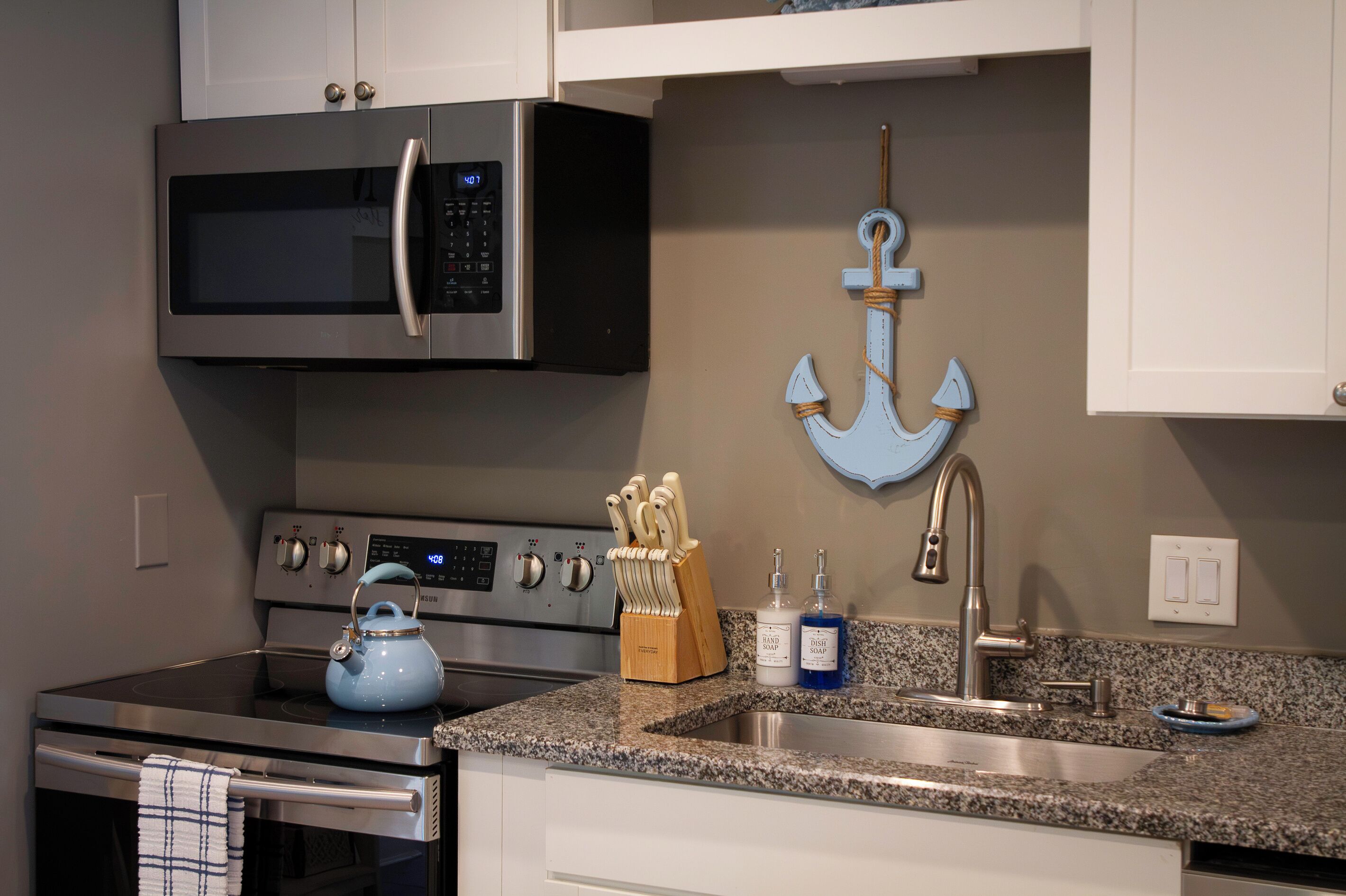 A kitchen with stainless steel appliances, a granite countertop, and a decorative anchor on the wall.