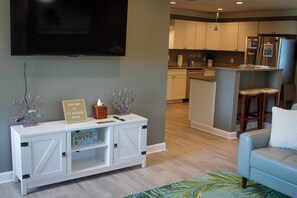 A modern living room with a white entertainment unit, a flat-screen TV, and a light blue armchair. - Private Pool, Fire pit, Pet-friendly Home (Panama City)