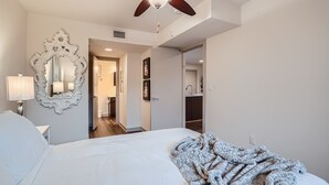 A bedroom with a large bed, a ceiling fan, a mirror, and a door leading to a bathroom.