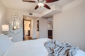 Quarto com cama grande, ventilador de teto, espelho e porta para o banheiro.