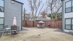 A backyard patio with a concrete floor, two chairs, a table, and a pink umbrella.