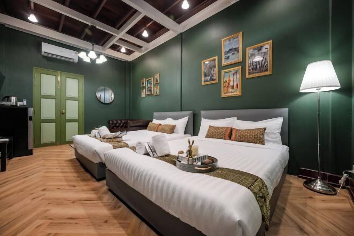 Une chambre d’hôtel avec deux lits, un mur vert, des tableaux encadrés, une lampe et un plancher en bois.