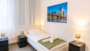 Ett hotellrum med en säng, två sängbord, ett fönster med tunna gardiner, en tavla som föreställer en stadsbild och två lampor.