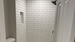 A bathroom with white subway tiles, a white toilet, and a shower with a white base. - Peaceful retreat in west Baltimore (Baltimore)