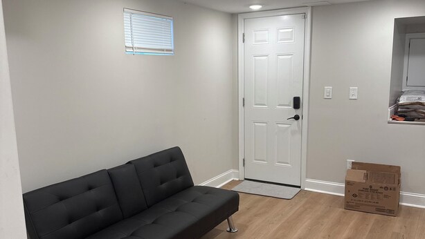 A room with a black sofa, a white door, wooden flooring, and a window with blinds. - Peaceful retreat in west Baltimore (Baltimore)