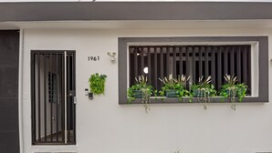 Une façade de bâtiment moderne, avec un revêtement extérieur blanc, une porte noire et une fenêtre dotée de stores verticaux.