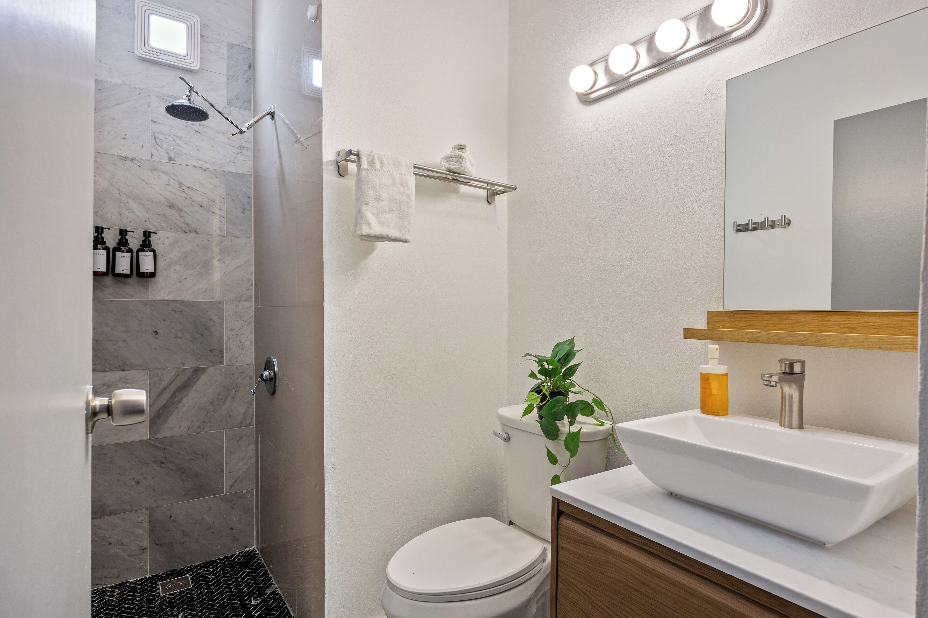 Een badkamer met douche, toilet, wastafel en spiegel.