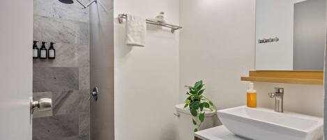 Een badkamer met douche, toilet, wastafel en spiegel.