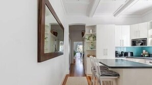 A modern kitchen with white cabinets, a large island with bar stools, and a long hallway leading to a dining area. - Dolphin Sands; A 3-bedroom apartment in Coogee Beach, barefoot walk to sand. (Coogee)