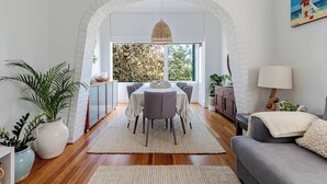 A dining area with a table and chairs, a sofa, and a lamp. - Dolphin Sands; A 3-bedroom apartment in Coogee Beach, barefoot walk to sand. (Coogee)