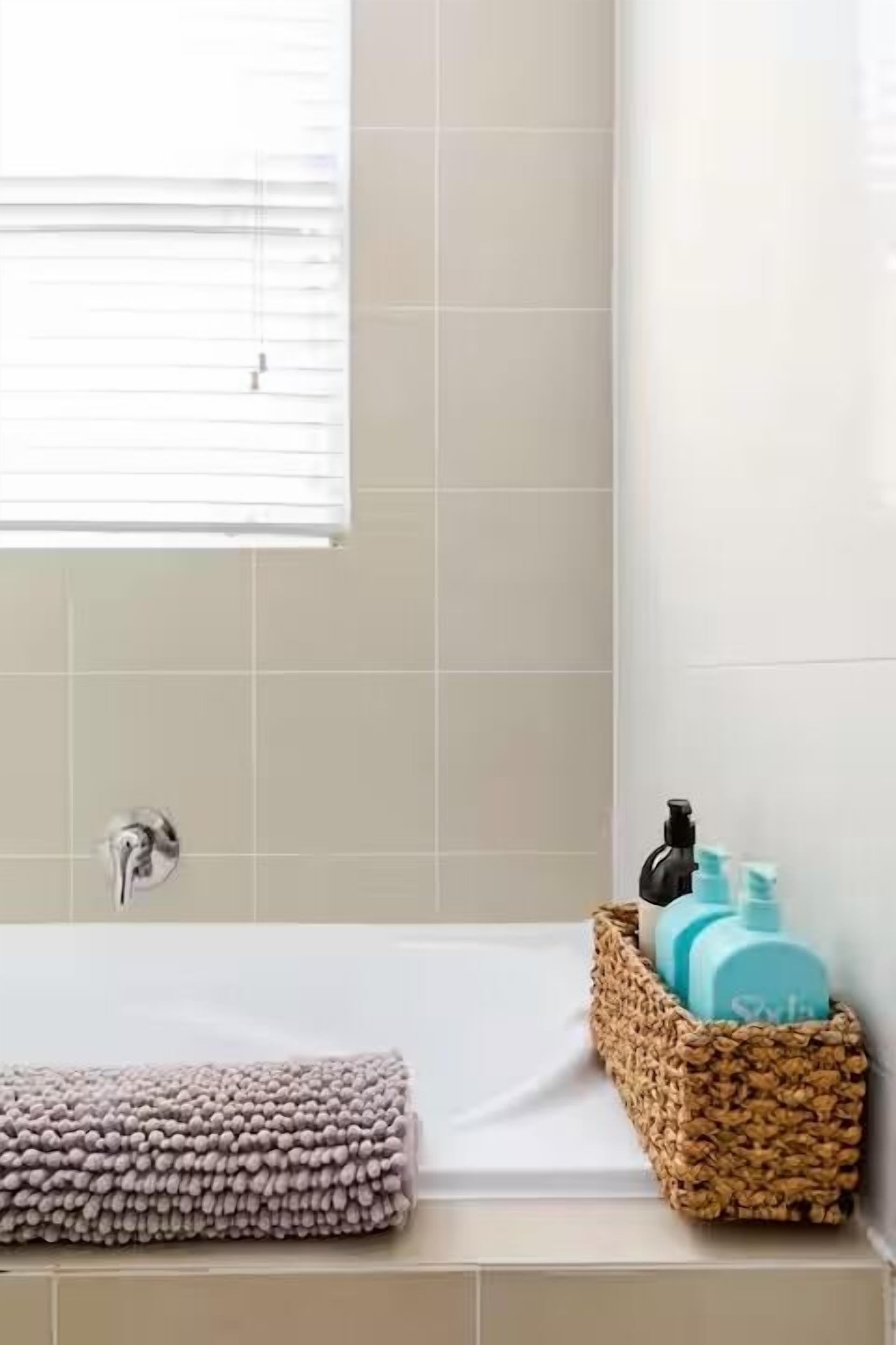 Un baño con bañera, una toalla y un cesto de artículos de aseo.