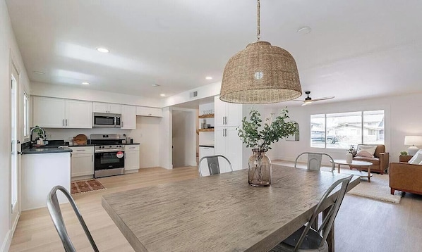 A modern kitchen with white cabinets, a dining table, and a hanging light fixture.