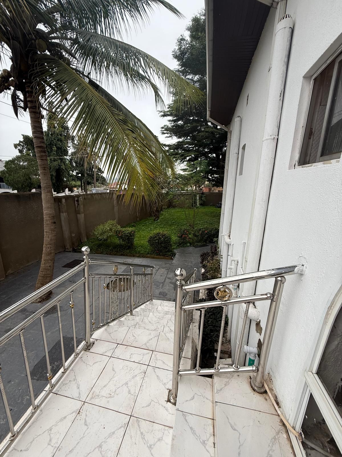 A staircase with metal railings leading to a building entrance, surrounded by a garden with a palm tree and other greenery.