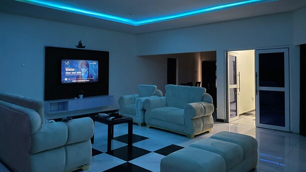 A modern living room with a flat-screen TV mounted on the wall, two light-colored sofas, a coffee table, and a checkered floor.