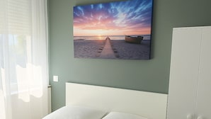 Una cama con sábanas blancas, cabecera y armario en una habitación con vista al atardecer sobre el mar.