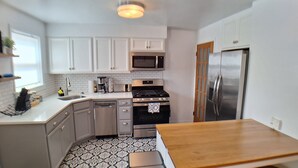 Una cocina compacta con armarios blancos, microondas, estufa, lavavajillas y refrigerador.