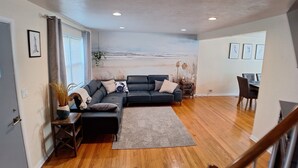 Una sala de estar moderna con un sofá de cuero oscuro, un tapete estampado y un comedor con mesa y sillas.