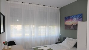 Un dormitorio ordenado con una cama, una mesa con un florero y un cuadro en la pared.