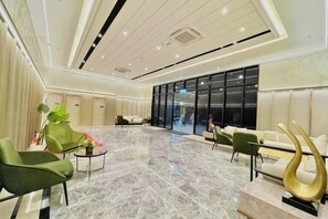 Un hall d’entrée spacieux avec un sol en marbre, des sièges verts et blancs, et un comptoir d’accueil moderne.