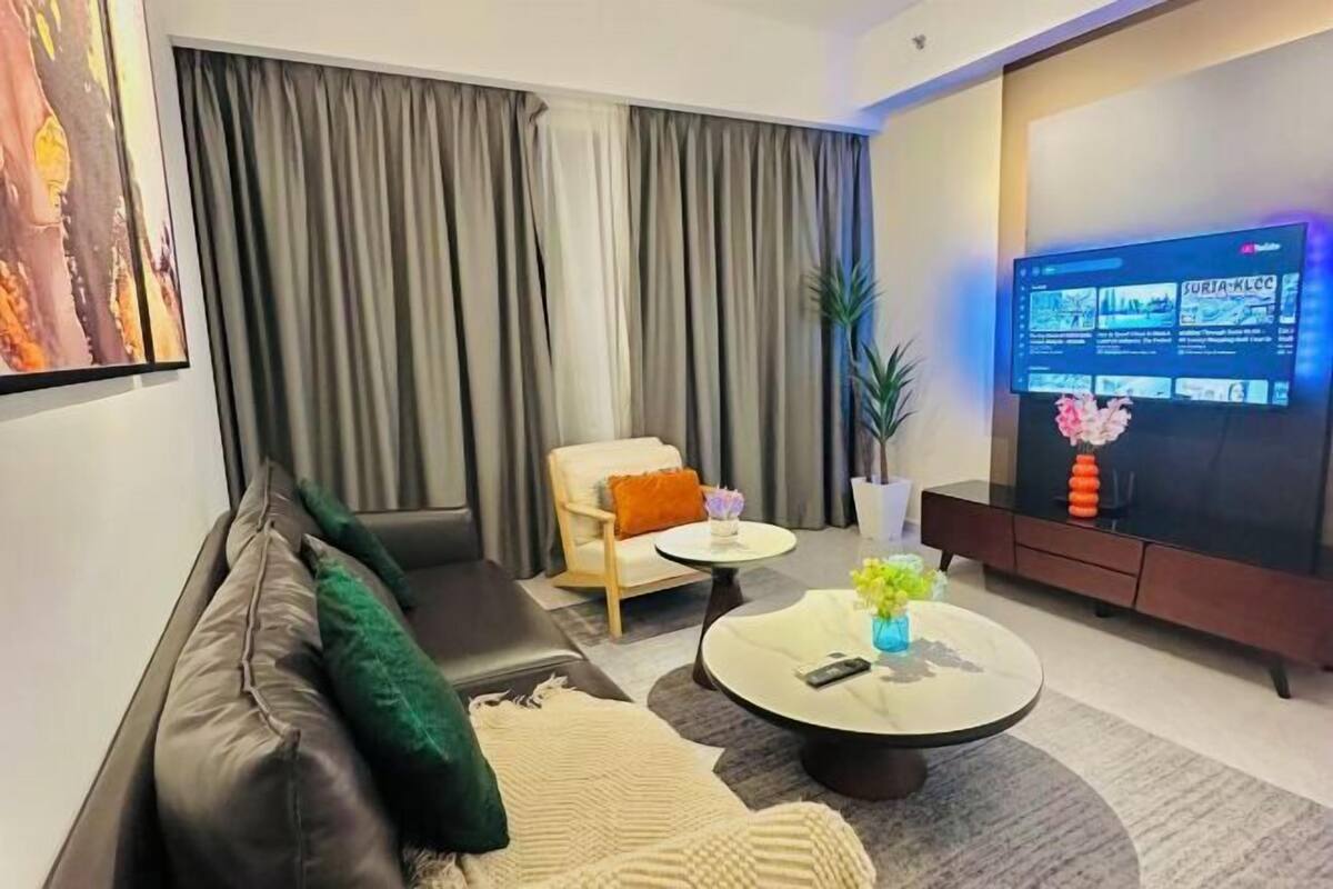Una sala de estar moderna con un sofá, un sillón, una mesita de centro y un televisor que muestra un programa.