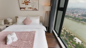 A hotel room with a bed, a view of a river, and a cityscape. - Masteri West Height - Vinhomes SmartCity - HanoiHomes (Hanoi)