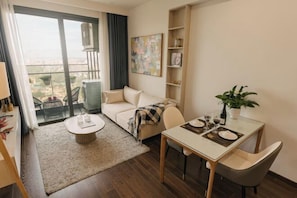 A modern living room with a sofa, a dining table, a coffee table, a bookshelf, and a balcony with a view.