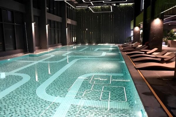 Une piscine intérieure avec un sol carrelé, des chaises longues et un intérieur aux couleurs sombres.
