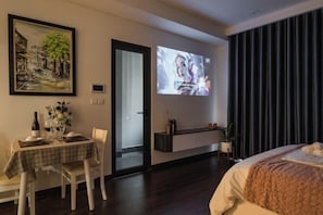 A hotel room with a dining area, a bed, a TV screen, and a painting on the wall.