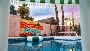 A pool area with a sign reading "PLUNGE INTO PARADISE" and palm trees. - Wellness Retreat • Sauna•Cold Plunge•Pool•Golf•Spa (Scottsdale)