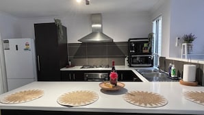A modern kitchen with a central island, a built-in stove, a microwave, and a sink. - Cosy White Retreat (Nollamara)