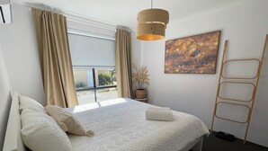 A bedroom with a large bed, a window with curtains, a hanging light fixture, a ladder, and a painting on the wall. - Cosy White Retreat (Nollamara)