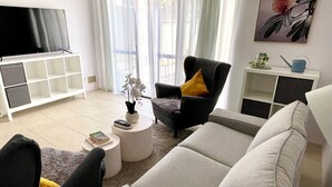 A living room with a sofa, armchair, and a TV on a stand. - Cosy White Retreat (Nollamara)