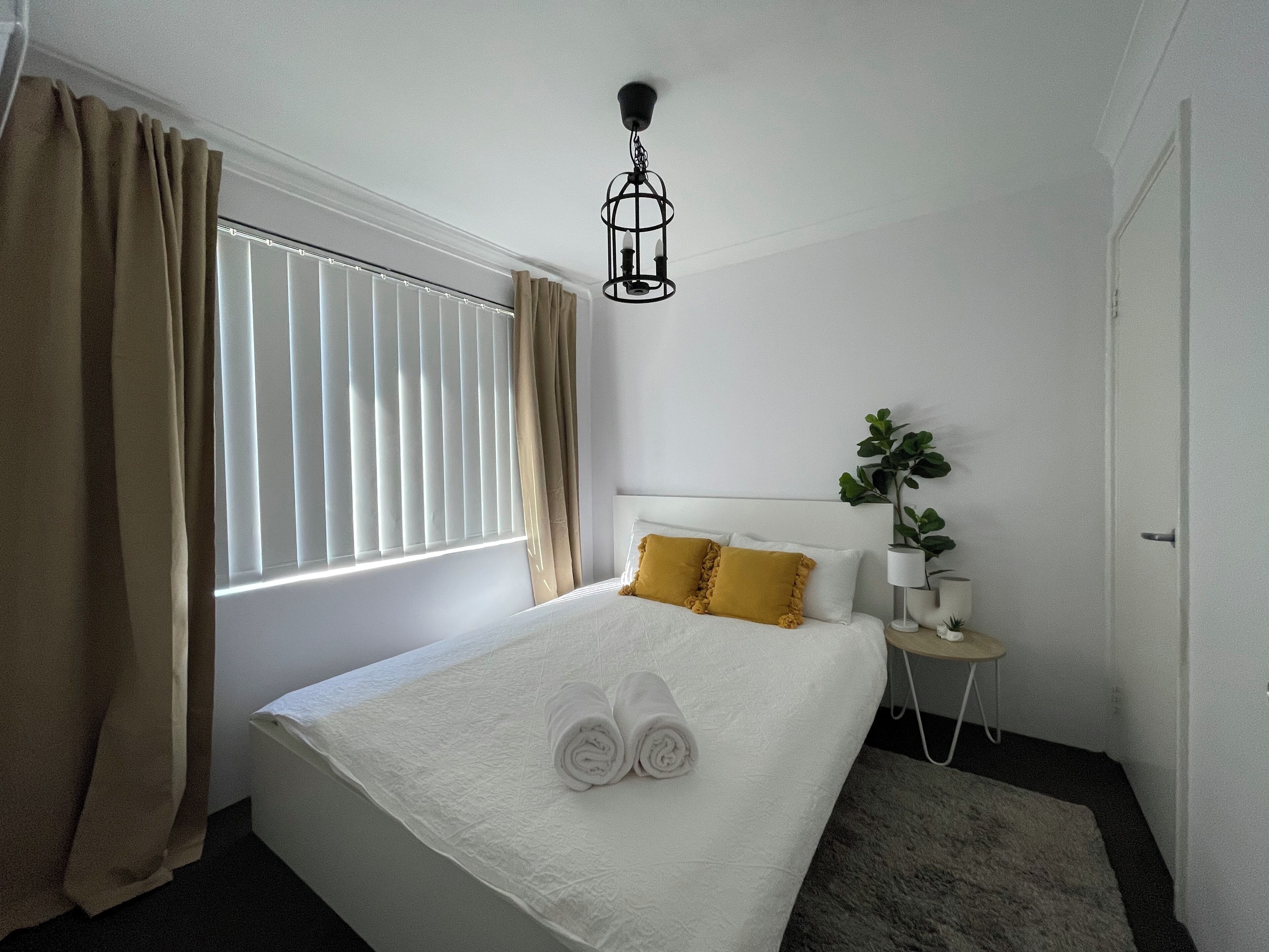 A hotel room with a bed, a bedside table, a lamp, and a potted plant.