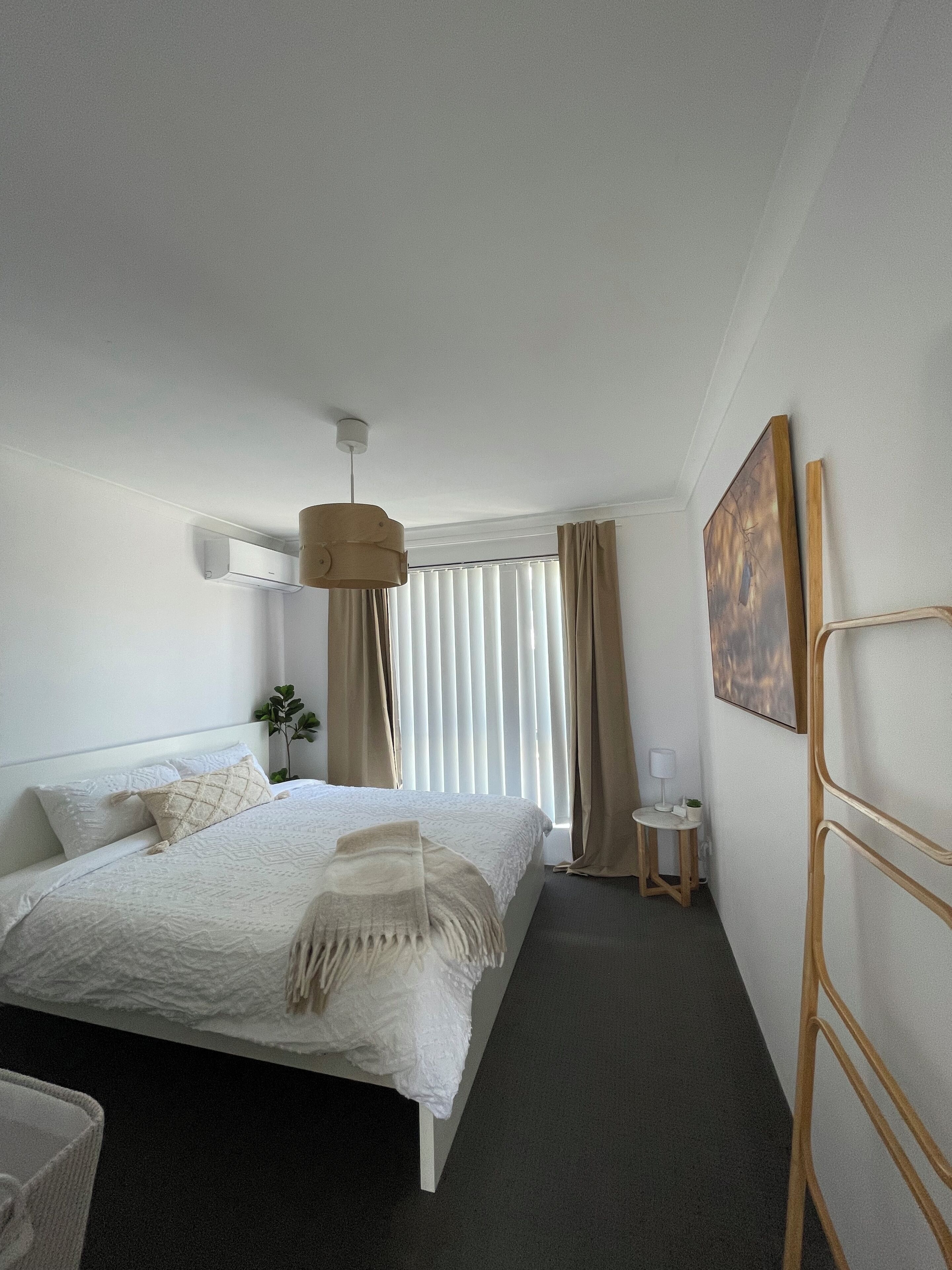A hotel room with a bed, a small side table, a lamp, and a painting on the wall.
