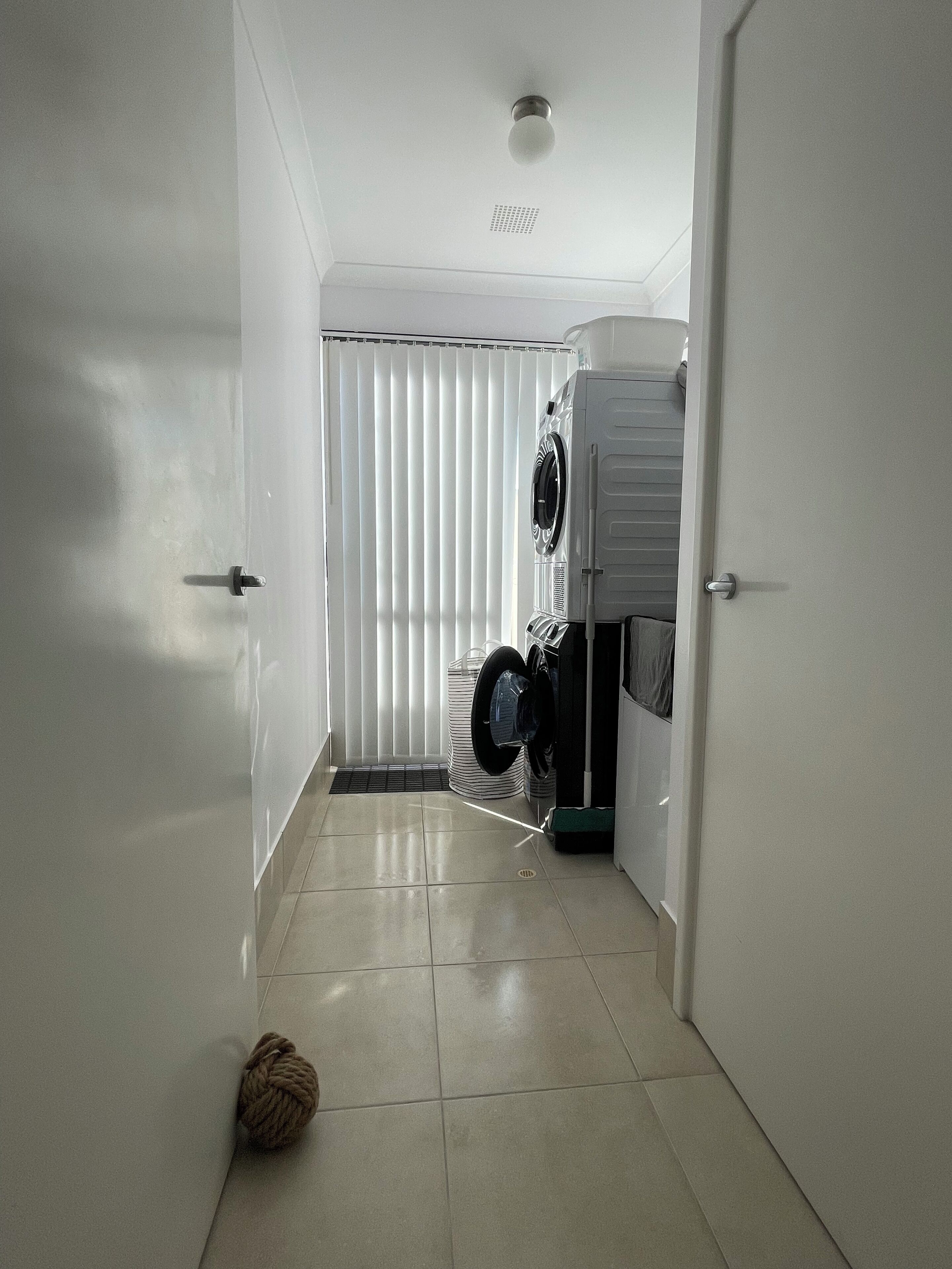 A narrow hallway with a washing machine and dryer, a door, and a ball of yarn on the floor.