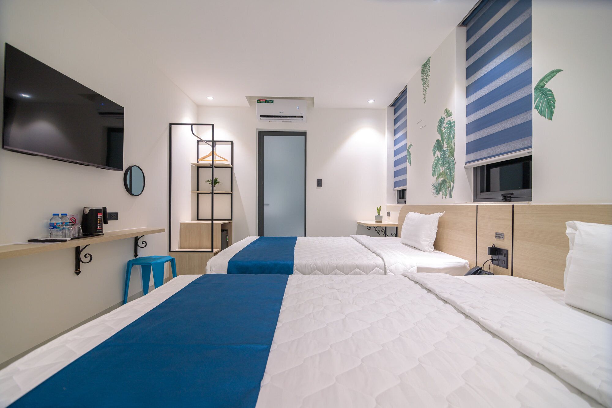 A hotel room with two beds, a desk with a chair, a TV, and a wall-mounted air conditioner.