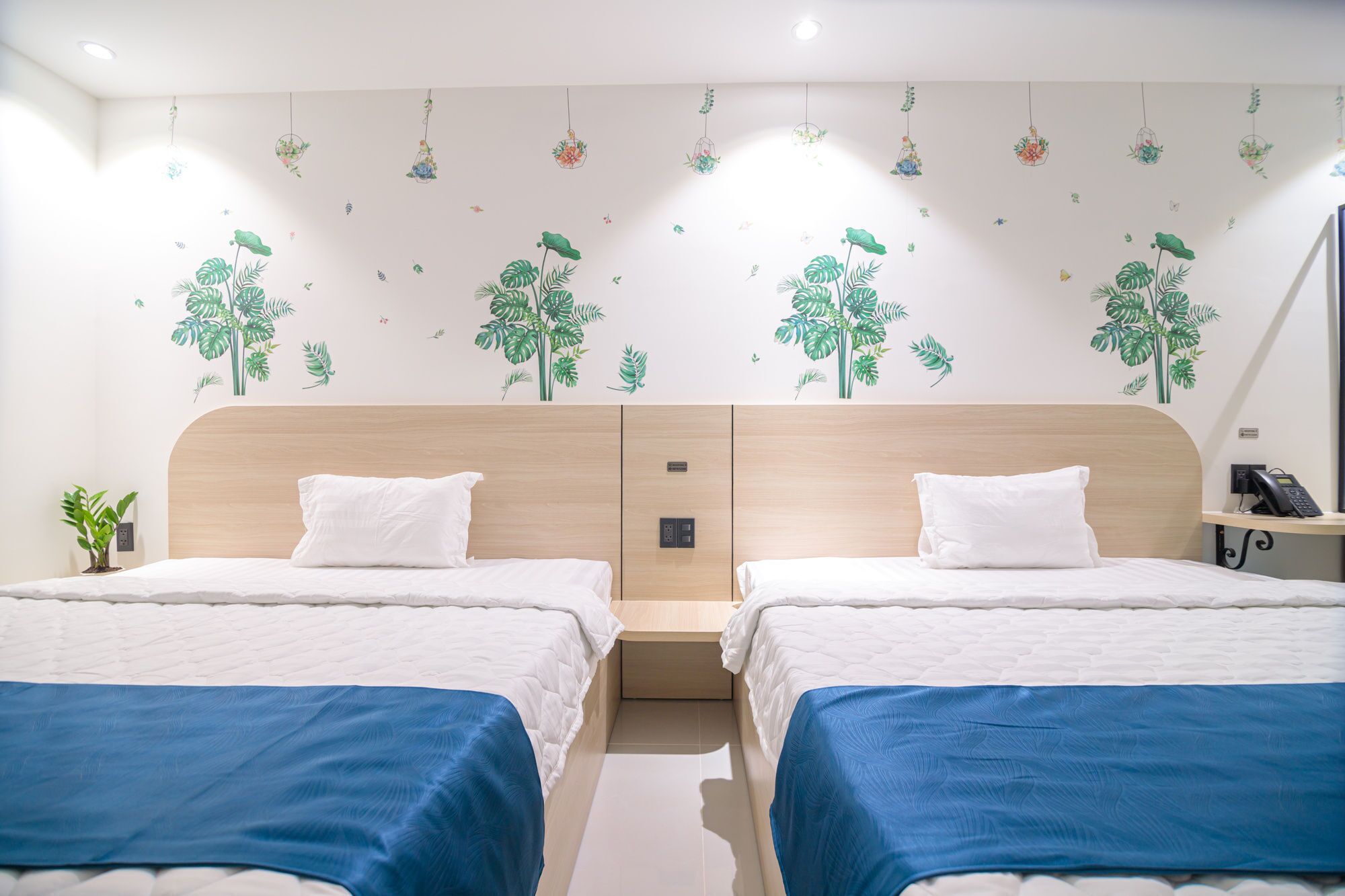 A hotel room with two beds, a wooden headboard, and a wall decorated with plant decals.