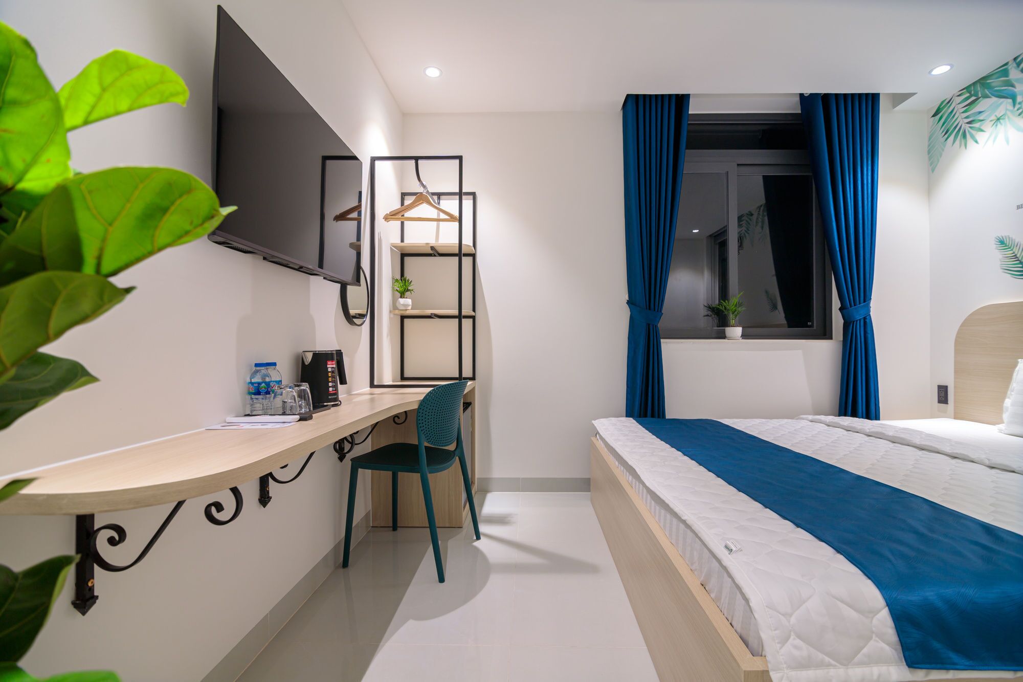 A modern hotel room with a desk, chair, bed, and a TV mounted on the wall.