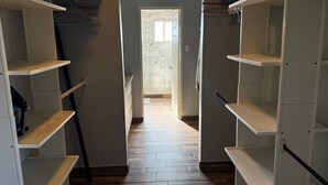 Um corredor estreito com piso de madeira que leva a uma porta. Estantes estão fixadas em ambos os lados do corredor.
